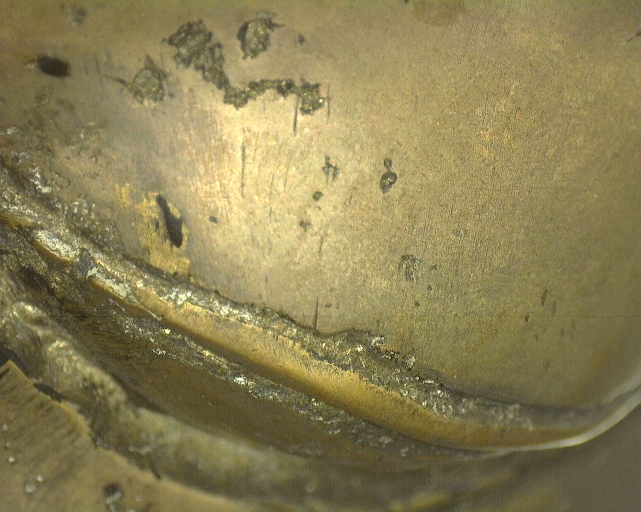 Forensic macro photograph of the brass-bronze casting skin with legitimate white-grey crystalline deposits in the deep mounting edges.