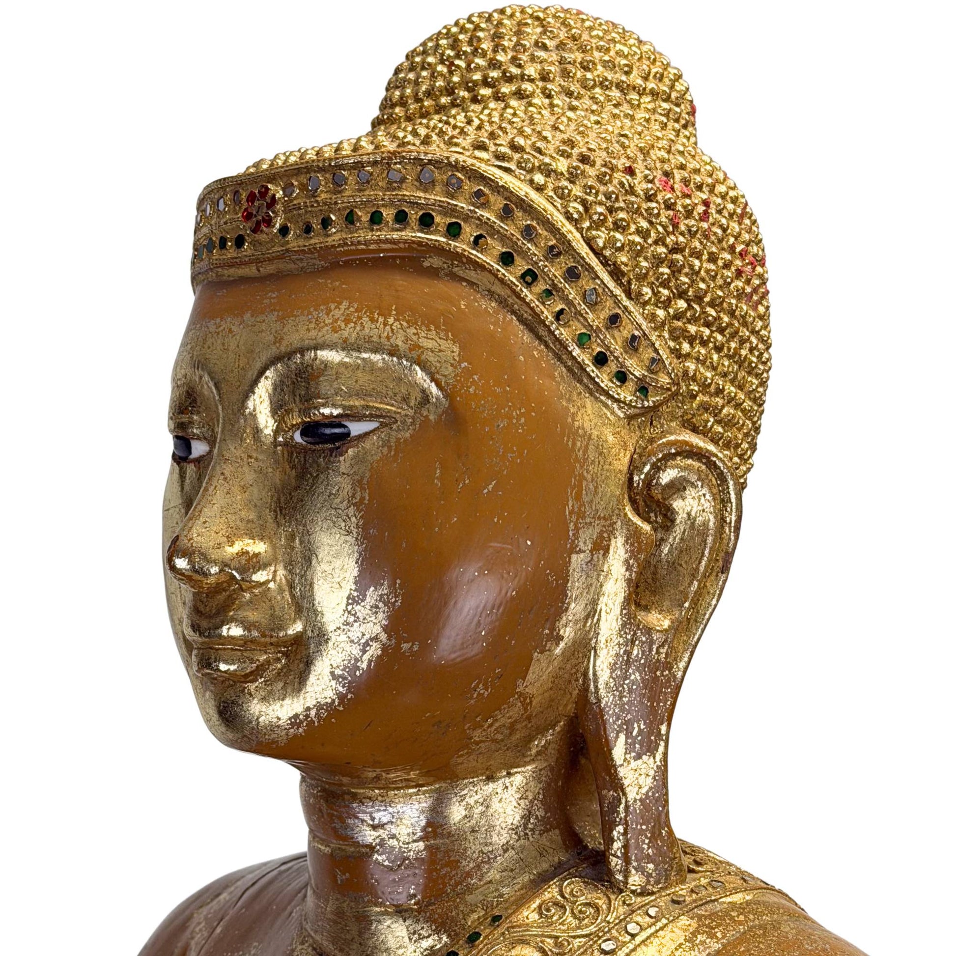Face of an antique Burmese Buddha with inlaid eyes, a golden headband, and a calm, meditative expression.
