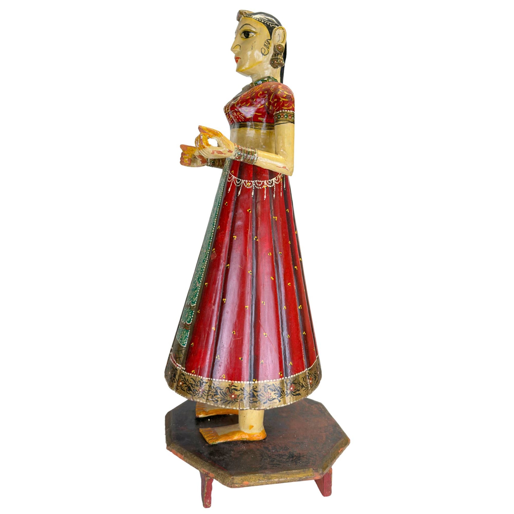 Hand-painted Chaniya Choli clothing on an Indian wooden statue with red lacquer, gold-colored patterns, and a green stripe.