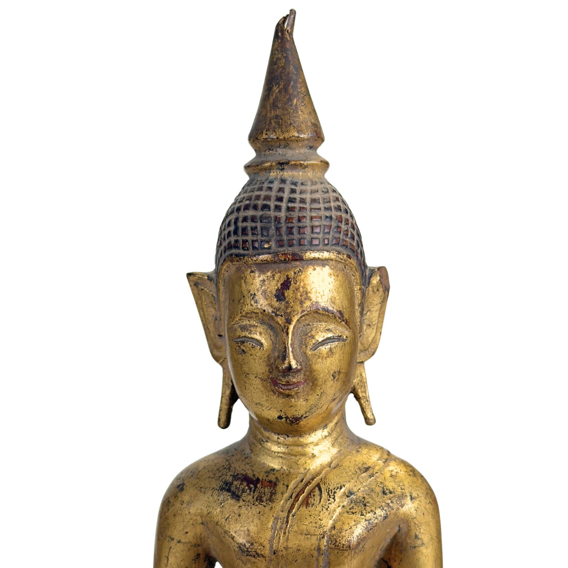 Detail of Lanna Buddha face with weathered gold leaf, dark wear, and subdued meditative expression