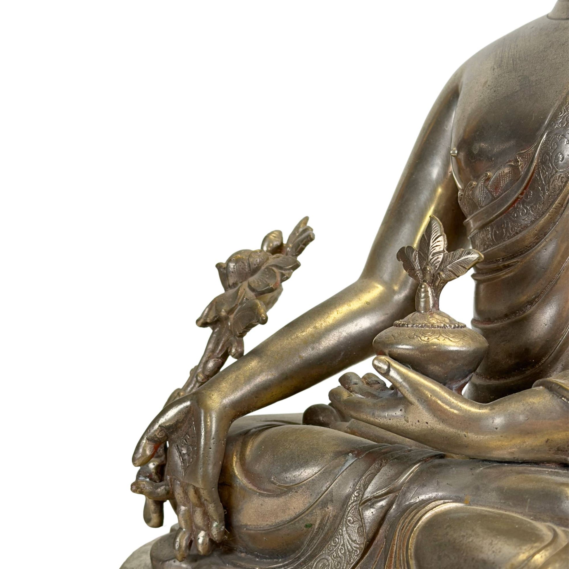 Detail of an antique Newar Bhaisajyaguru in silver-plated bronze with medicine pot, myrobalan plant, finely engraved robes, and natural wear that underscores its great age.