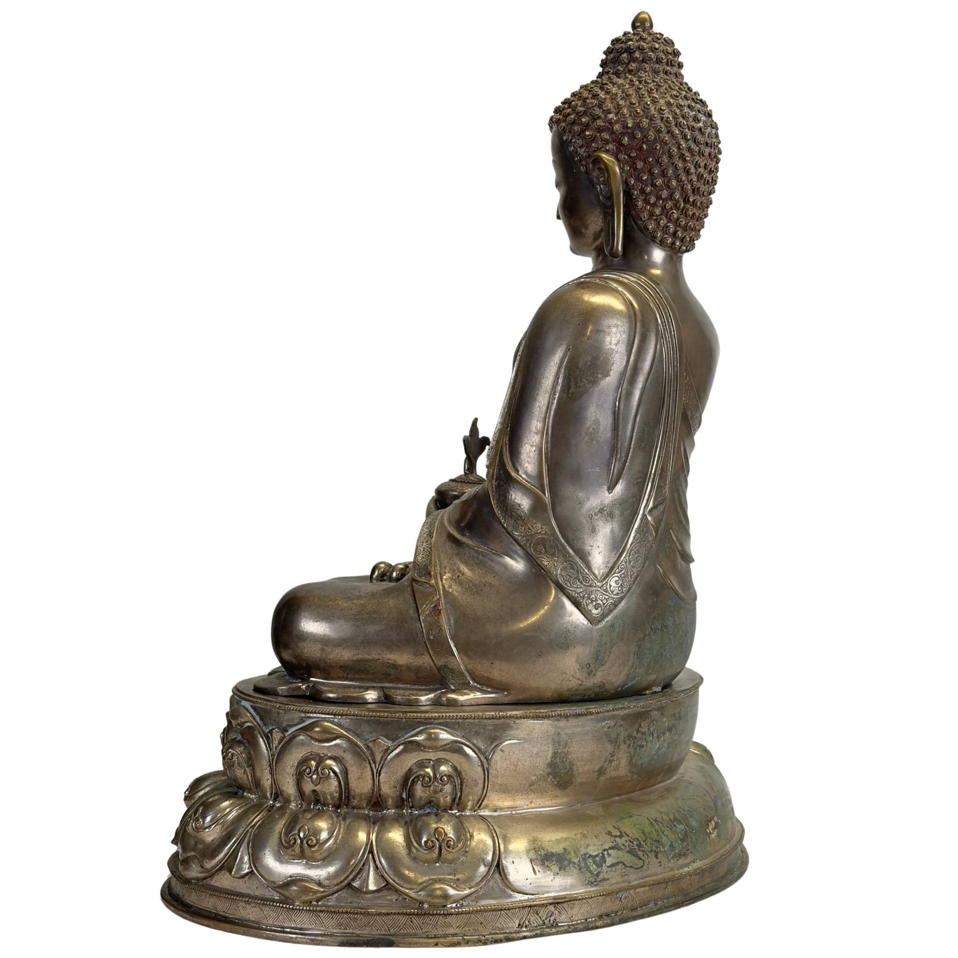 Left side of an antique Newar Bhaisajyaguru in silver-plated bronze on a two-part lotus throne, with natural patina, engraved monk's robe, and wear consistent with great age.