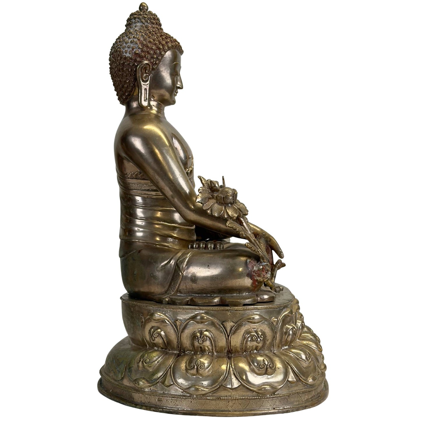 Left side view of an antique Newar Bhaisajyaguru in silver-plated bronze on a richly chased double lotus throne with a medicinal plant and natural patina.