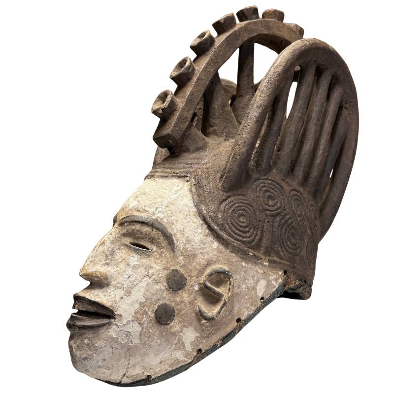 Old African mask with white patina, hand-carved ritual object with dark headdress and spiral ornaments